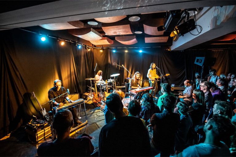 Een muziekgroep optredend voor een publiek in een sfeervolle, verlichte zaal.