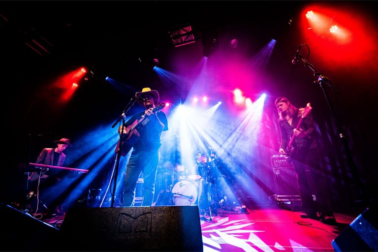 Een band speelt live op een podium met kleurrijke lichten en visueel indrukwekkende verlichting.