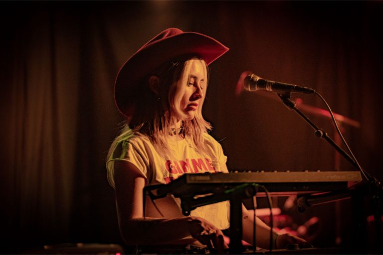 Een muzikant in een cowboyhoed speelt keyboards op het podium.