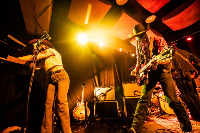 Een band speelt live muziek op een podium met kleurrijke verlichting.