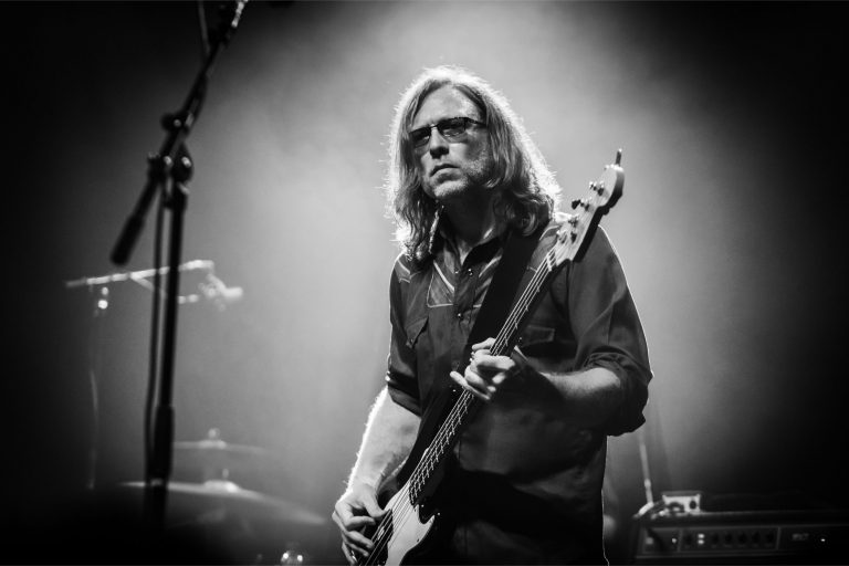 Een muzikant speelt basgitaar op het podium onder sfeerverlichting.