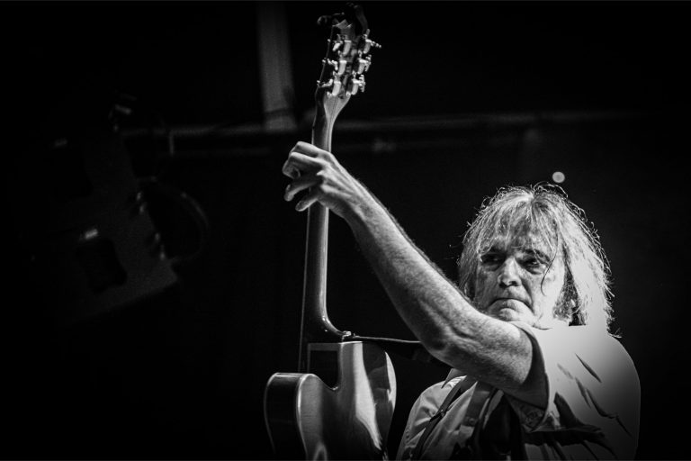 Zwart-wit afbeelding van een muzikant die gefocust zijn gitaar bespeelt.