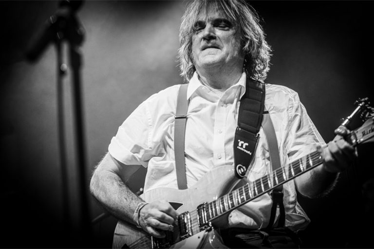 Een muzikant speelt gitaar op een podium in zwart-wit.