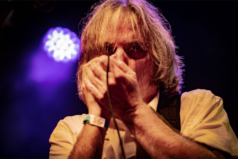 Een muzikant speelt harmonica op het podium met gekleurde lichten op de achtergrond.