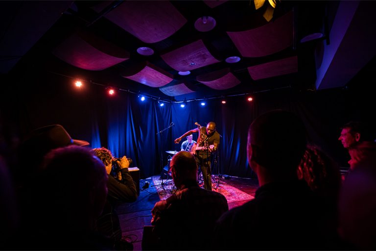 Een muzikant optredend op het podium met kleurrijke verlichting voor een publiek.