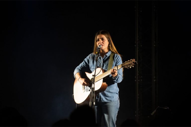 Een muzikant die een akoestische gitaar bespeelt op een donkere podium.