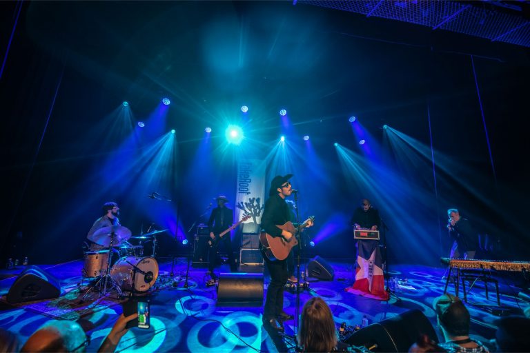 Een band speelt live op het podium met blauwe verlichting en een sfeervolle achtergrond.