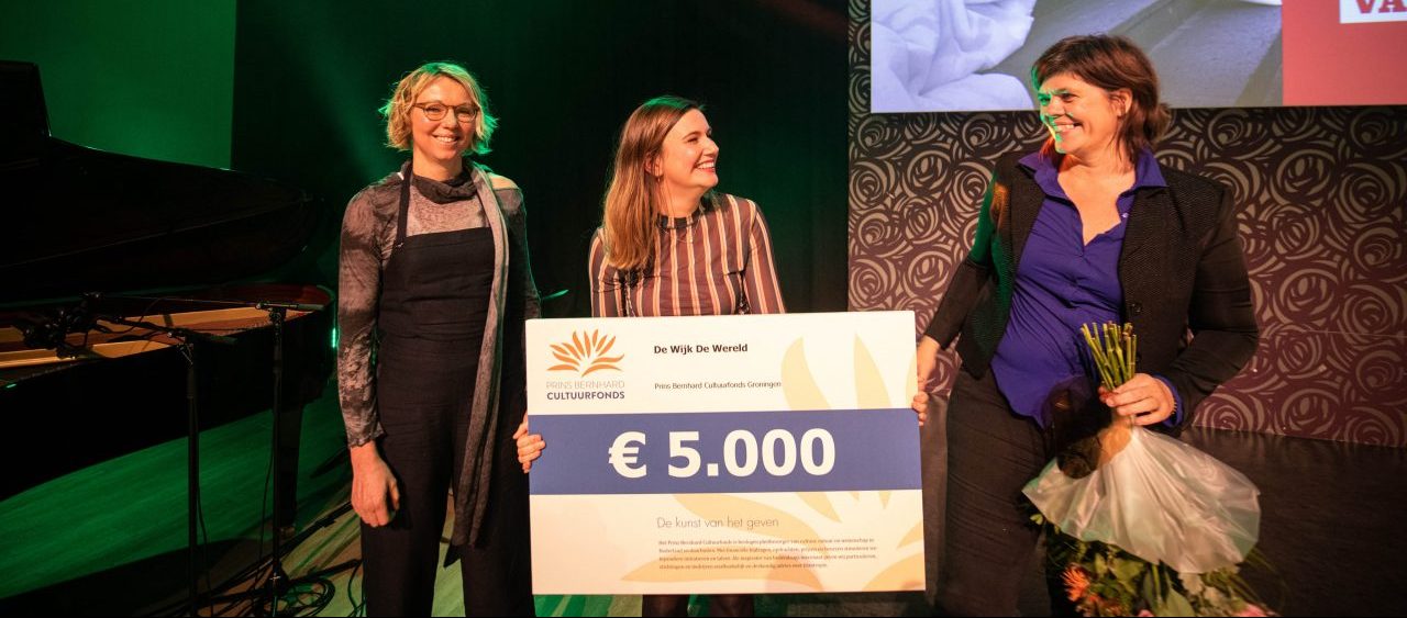 Drie vrouwen staan op het podium en houden een cheque van € 5.000.