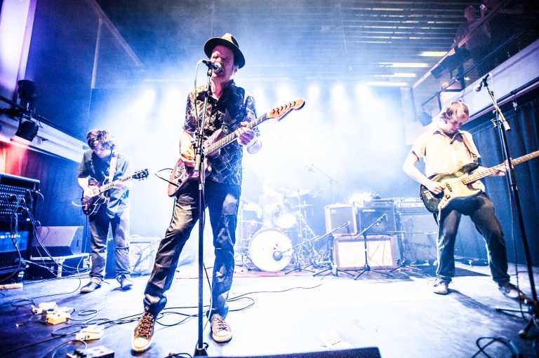 Een bandoptreden met vier muzikanten op een verlichte scène.