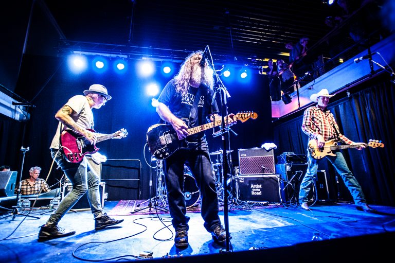 Een band speelt live op een podium met blauwe verlichting.