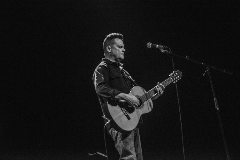 Een muzikant staat op het podium met een gitaar en zingt in een microfoon.