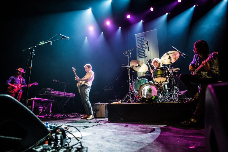 Een liveband speelt op het podium met kleurrijke lichten en een drummer in actie.