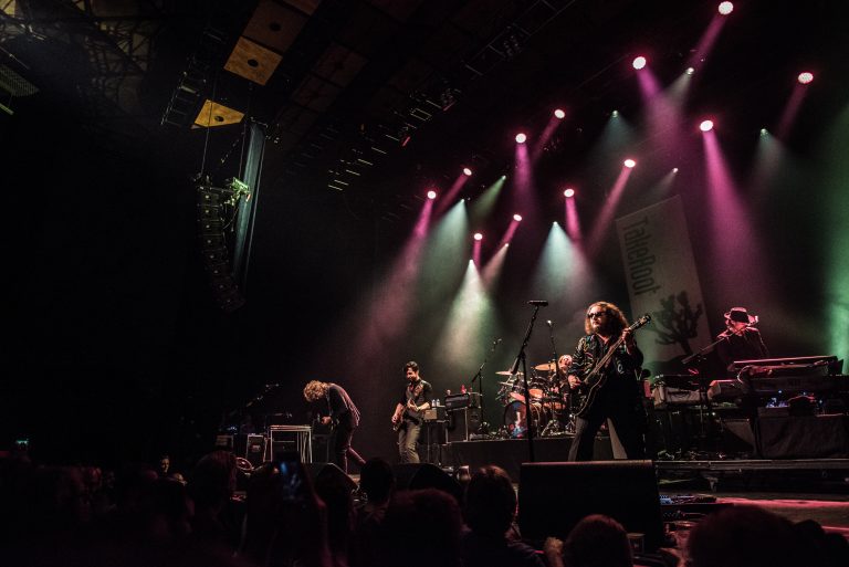 Een muzikale live-optreden op een podium met meerdere bandleden en kleurrijke lichten.