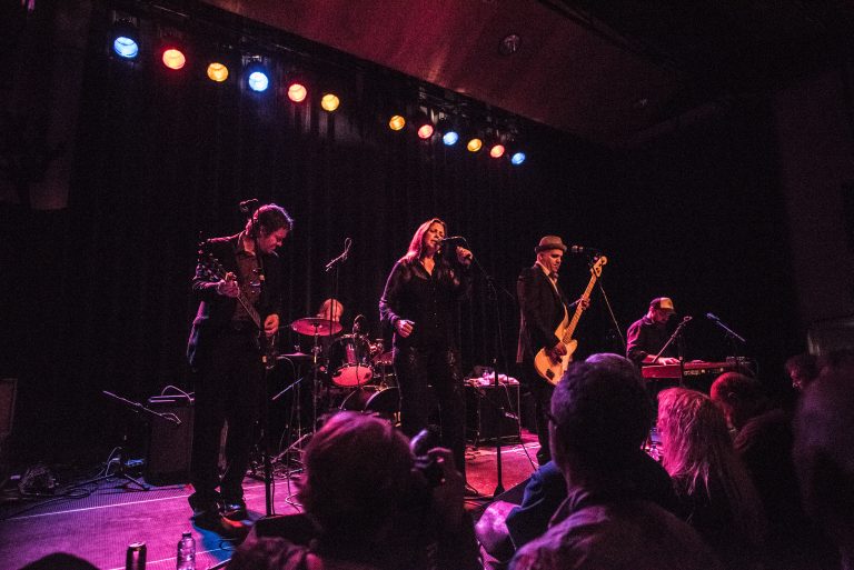 Een liveband performt op een podium met kleurrijke lichten, terwijl het publiek aan het genieten is van de muziek.