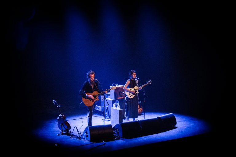 Twee muzikanten optreden op een podium met blauwe verlichting.