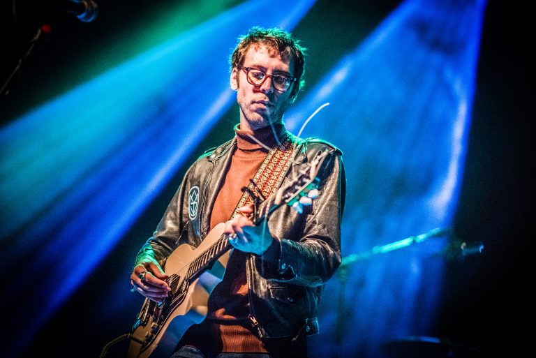 Muzikant speelt gitaar met kleurrijke lichtstralen op de achtergrond.