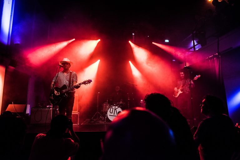 Een band speelt op een podium met felrood en paarse lichtjes.