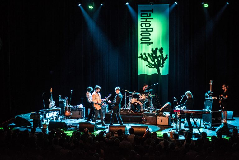 Een band speelt op een podium met groene belichting en een achtergrondbanner met het woord