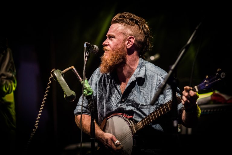 Een muzikant met een baard speelt banjo op het podium.