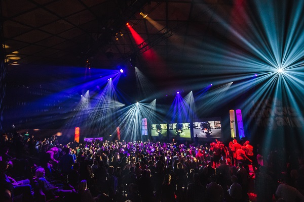 Een levendige sfeer met kleurrijke lichten en een menigte mensen tijdens een evenement of concert.