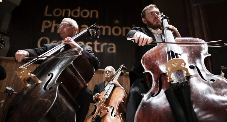 Drie muzikanten van een orkest spelen cello op het podium.