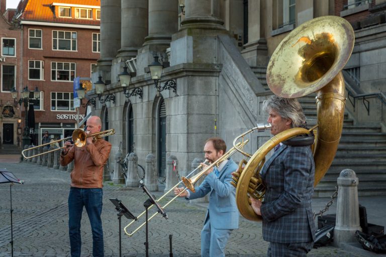 Drie muzikanten spelen samen op een straat, met een trompet, trombone en tuba.