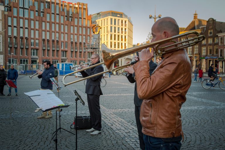 Een groep muzikanten speelt live op een plein, met een trombonist op de voorgrond.