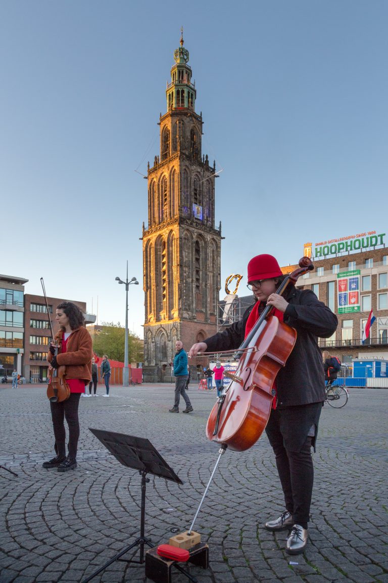 Straatmuzikant in een plein met een toren op de achtergrond.