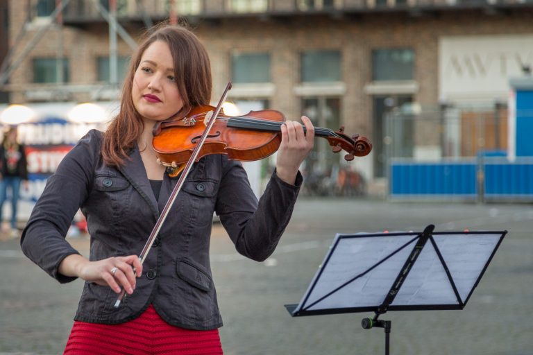 Een vrouw speelt viool op straat met een muziekstandaard naast haar.