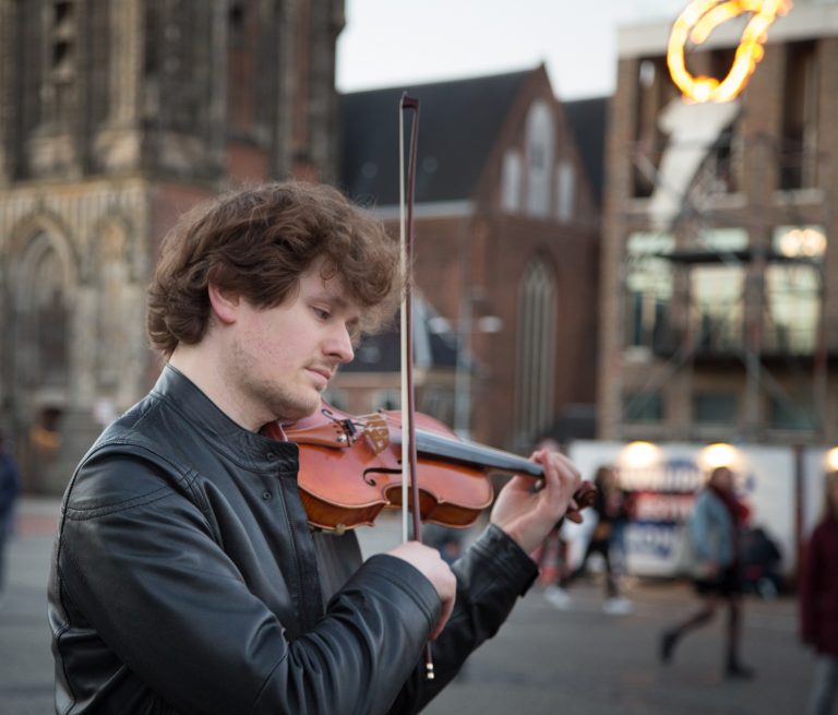Een jonge man speelt viool op straat met een levendige achtergrond.