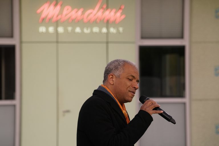 Een man met een microfoon zingt op straat voor een restaurant met de naam