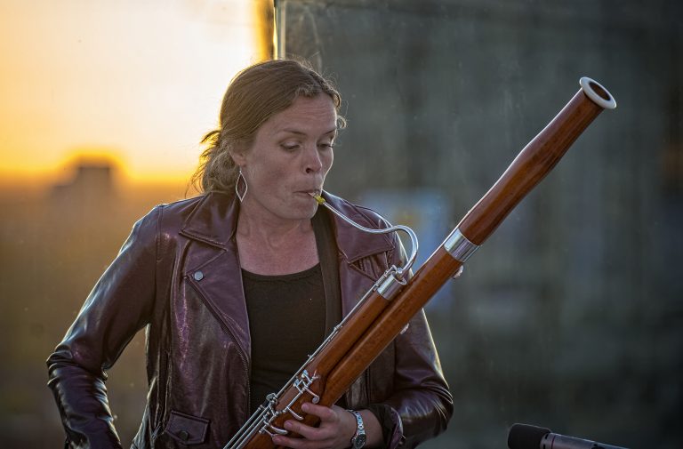 Een vrouw speelt een fagot tegen een achtergrond van een ondergang van de zon.