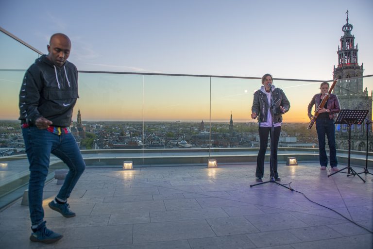 Drie muzikanten voeren een live optreden uit op een dakterras tijdens de zonsopgang.