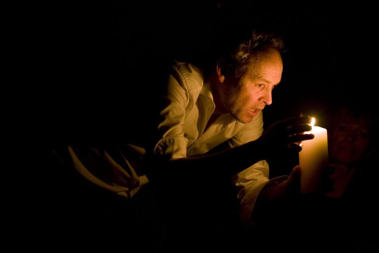 Een persoon met een lichtgevende kaars in een donkere omgeving, gefocust op het licht.