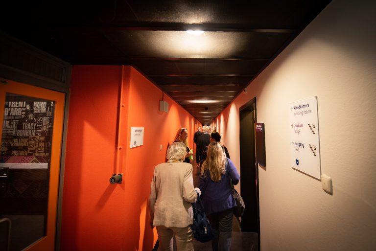 Een groep mensen loopt door een smalle gang met oranje muren.