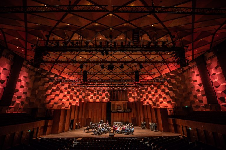 Een uitzicht op een concertzaal met een verhoogd podium, waar muzikanten optreden onder een indrukwekkend, gewelfde plafond.