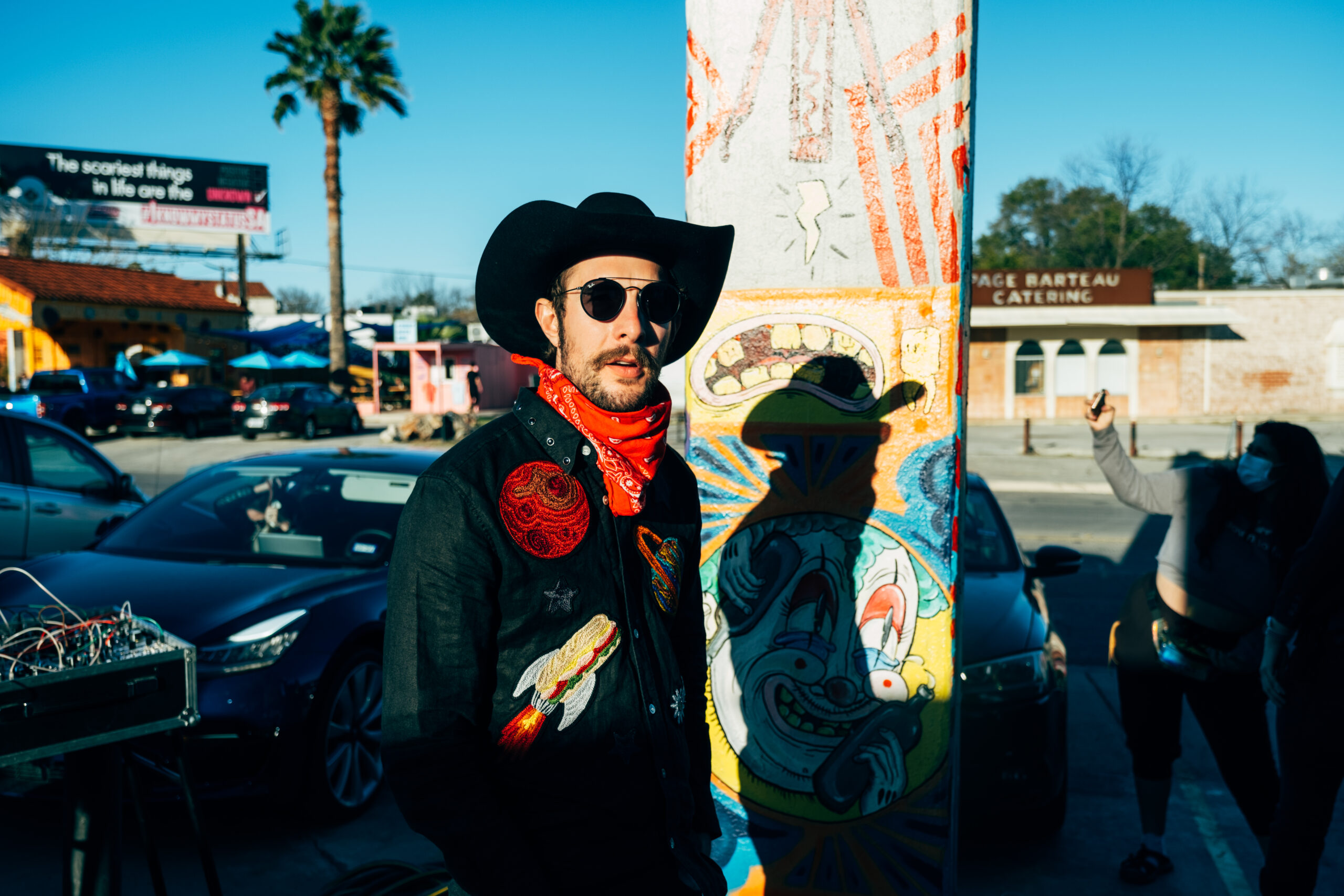 Garrett T. Capps staat met een zonnebril, hoed en een rode bandana op straat