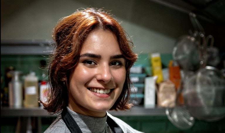 Vrouw met een vriendelijke glimlach, die in een keuken staat.