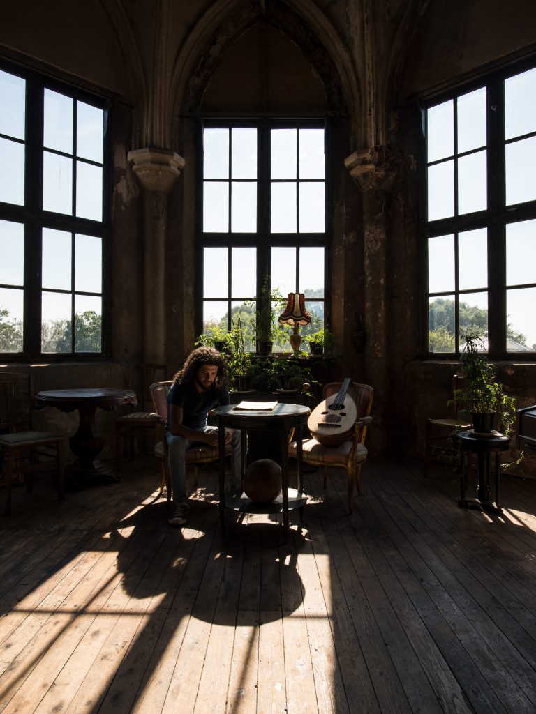 Een persoon zit aan een tafel in een kamer met grote ramen die veel natuurlijk licht binnenlaten.