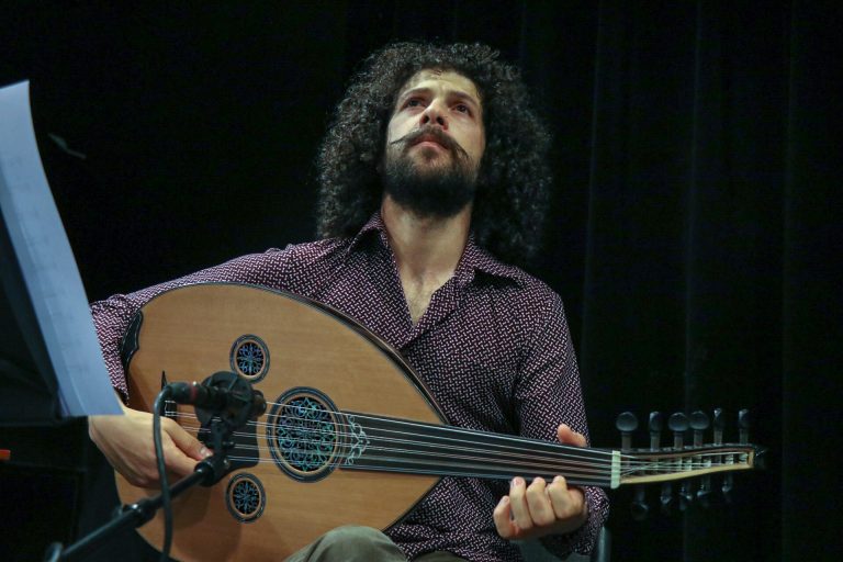 Een muzikant speelt op een Arabische luit (oud) terwijl hij omhoog kijkt.