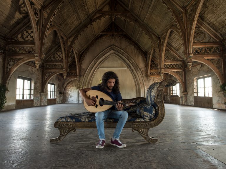 Een muzikant speelt op een luit in een grote, lege zaal met hoge, versierde plafonds.