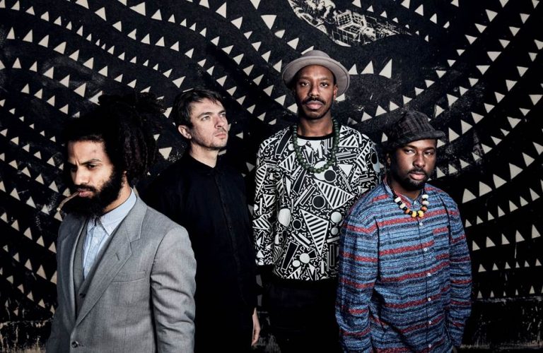 Een groep van vier mannen poseert voor een grafische achtergrond met geometrische patronen.