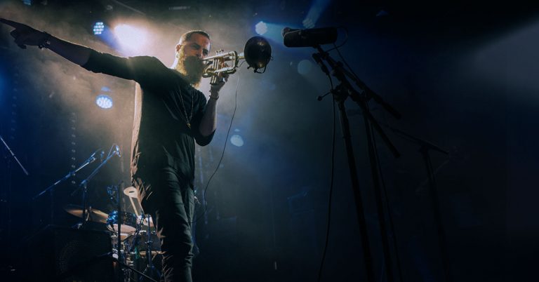 Een muzikant houdt een microfoon vast terwijl hij optreedt op een podium, omringd door sfeervolle verlichting.