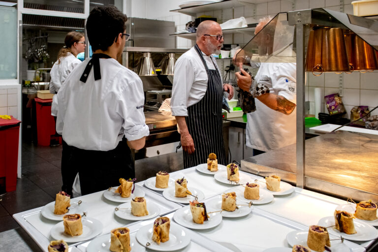 Koks en leerling koks tijdens event in de keuken met een tafel vol voorgerechten