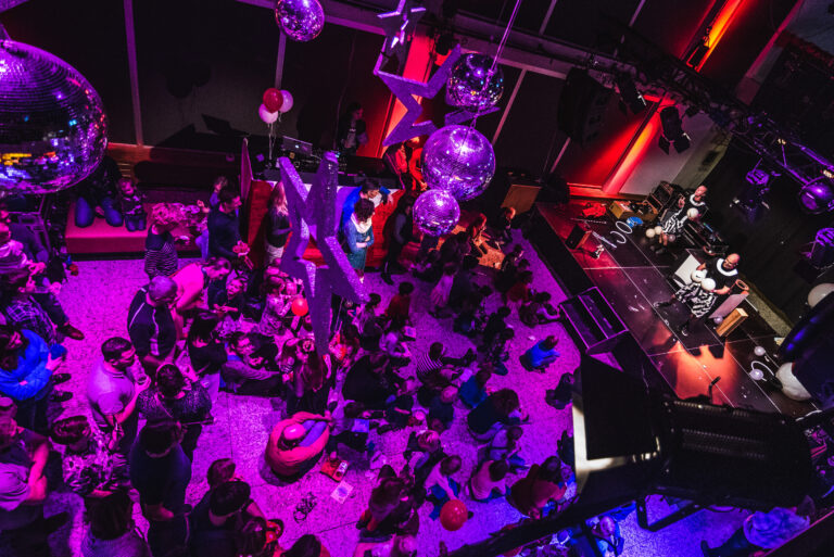 Gemengd publiek kijkend naar twee artiesten op het podium.