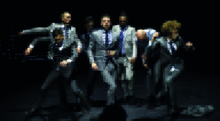 Een vaag en onscherp beeld van een groep mensen in formele kleding, waarschijnlijk een vergadering of evenement.