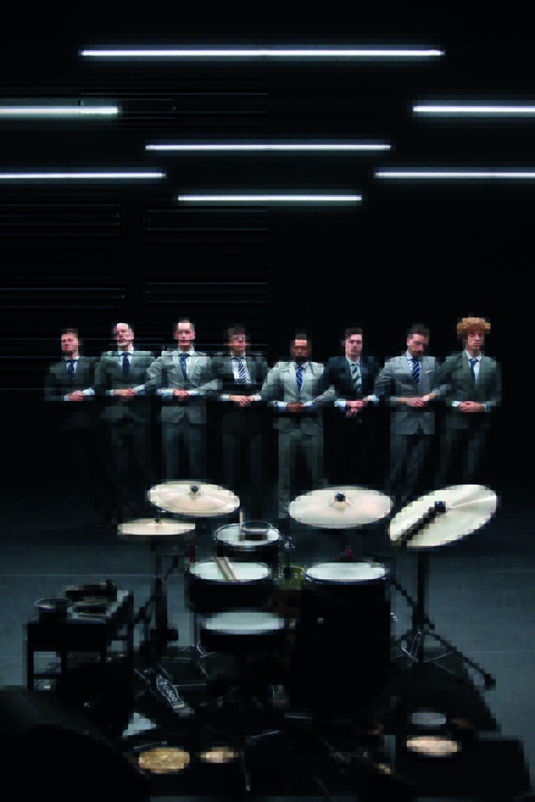 Een groep mensen in zakelijke kleding staat achter een drumstel, met een abstracte en vervormde achtergrond.