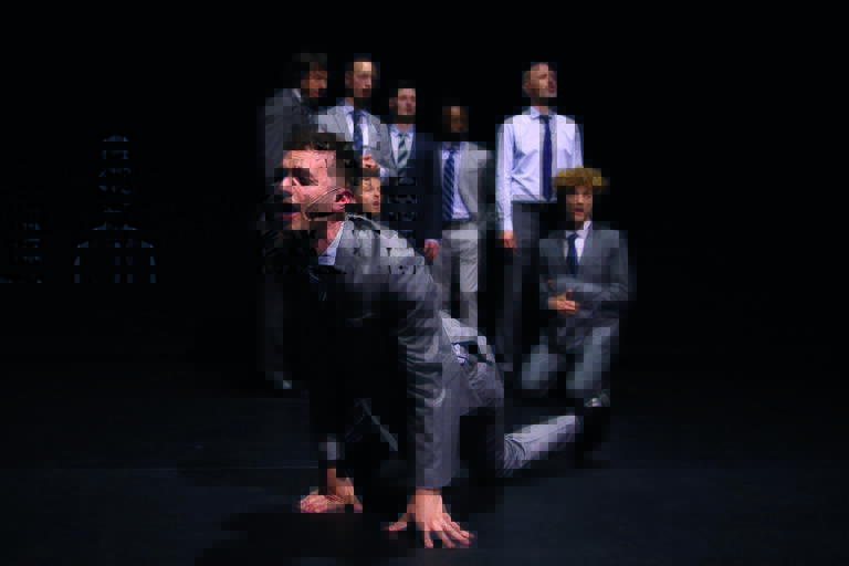 Een blurry afbeelding van een groep mensen, terwijl een man op handen en knieën voor hen op de grond zit.