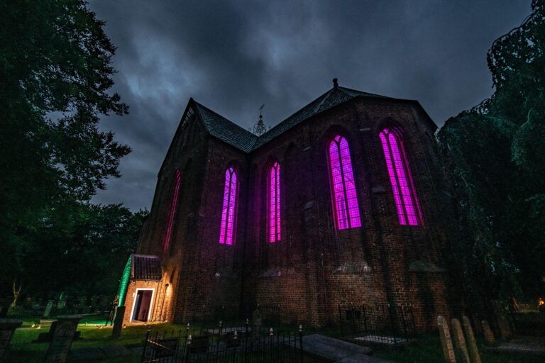 Een oude kerk met hoge, gekleurde ramen die paars licht uitstralen tegen een bewolkte lucht.
