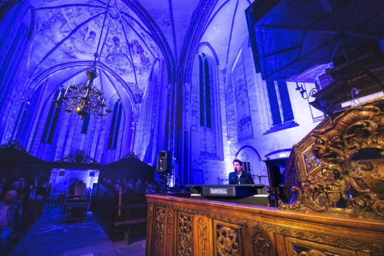 Een DJ staat achter een mengpaneel in een mooi verlichte kerk met blauwe en paarse verlichting.